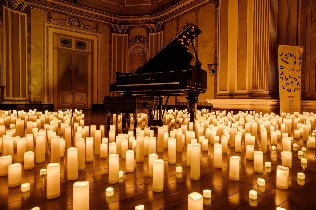 A photograph of a piano in an ornate room with candles covering the wooden floor.