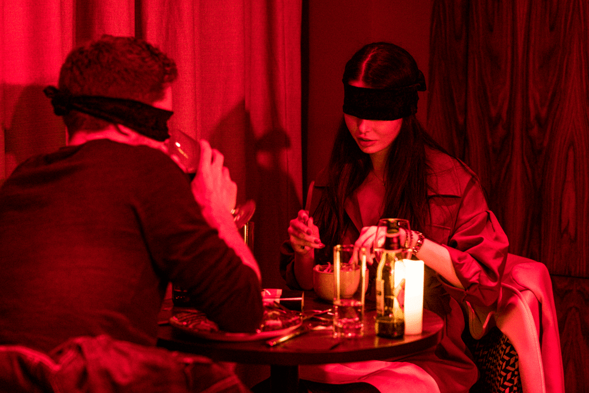 Una pareja con los ojos vendados cenando en un ambiente íntimo: la experiencia Dining in the Dark en Los Ángeles.