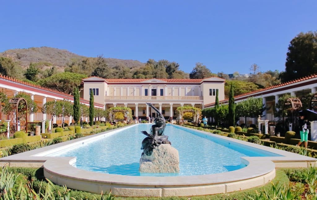 A view of the Getty Villa courtyard with a pool of water and sculpture. 