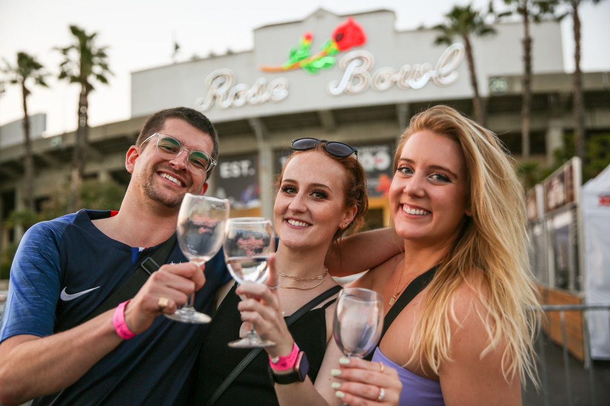 Two women and a man stand outside the Rose Bowl and toast glasses of rose