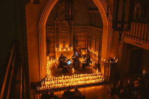 A string quartet plays music in a church surrounded by candlelight