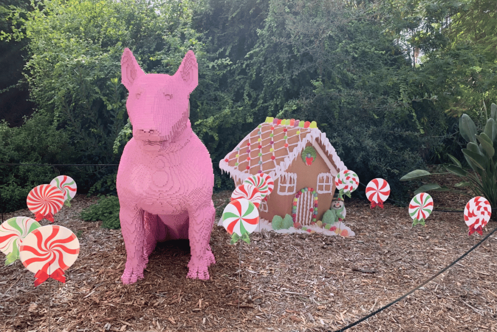 A pink LEGO sculpture of a dog next to a gingerbread house