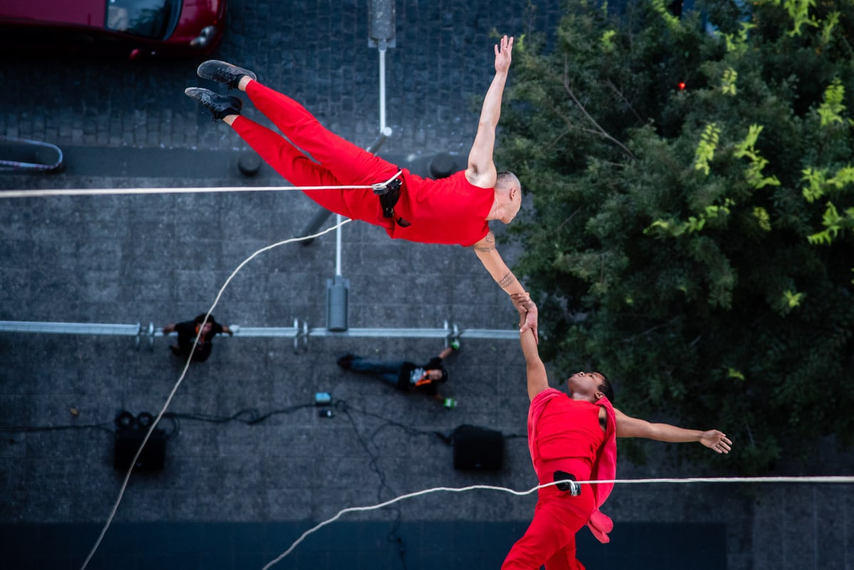 Two suspended dancers move across the front of a building
