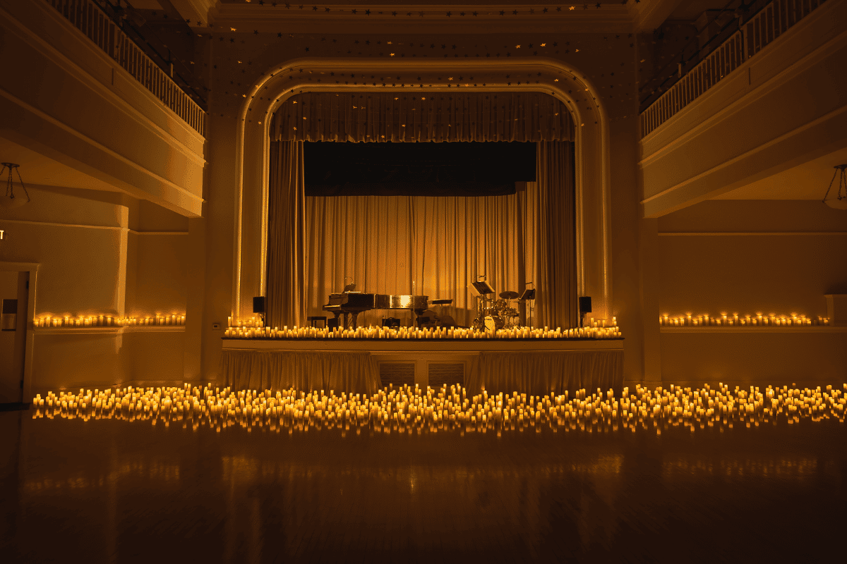 A Candlelight concert set up inside Santa Monica Bay Woman's Club with candles in front of the stage and more on the stage where a piano and other instruments rest under the open arched wall.
