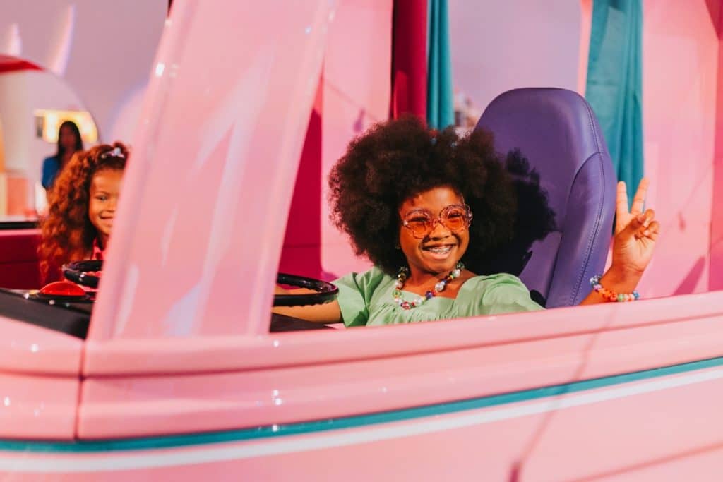 A young girl sits in a pink Barbie Camper Van