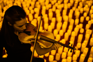 above shot of violinist performing on stage while surrounded by hundreds of candles