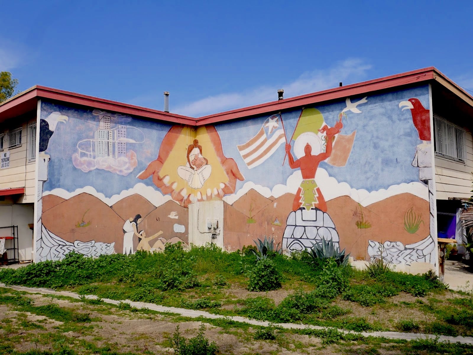 A mural is painted across two walls showing a man holding Mexican and American flags