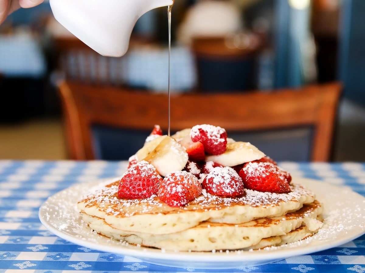 A stack of fluffy pancakes with strawberries and bananas on top drizzled with syrup at John O'Groats in Los Angeles.