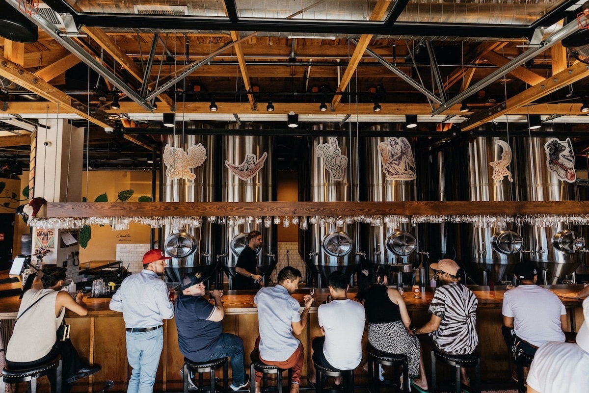 A group of people sitting at a counter at a brewery. 