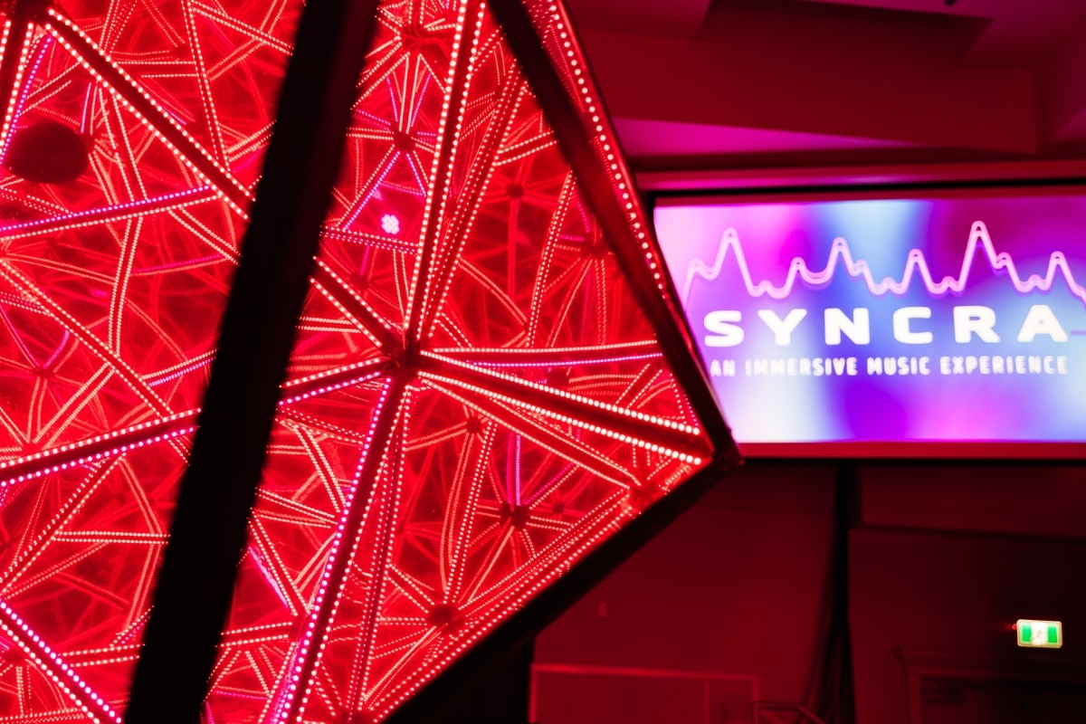 An illuminated sculpture sits in front of a sign for SYNCRA