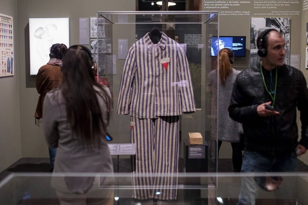 A striped uniform worn by concentration camp victims hangs in a display case