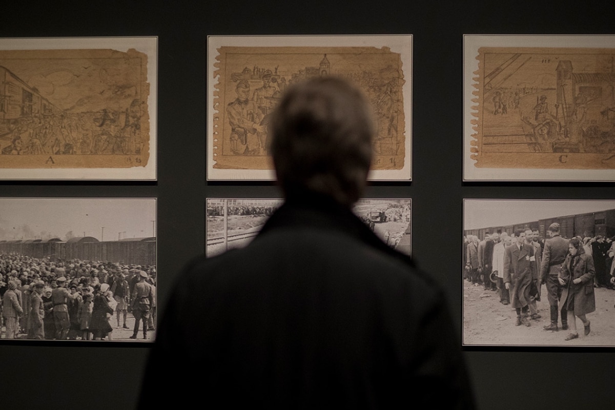 A man looks at a wall of photos of Auschwitz