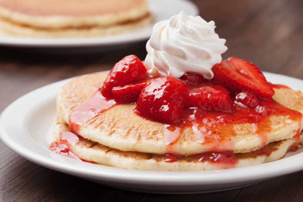 image of NORMS Restaurants pancakes / hotcakes topped with strawberries and whipped cream