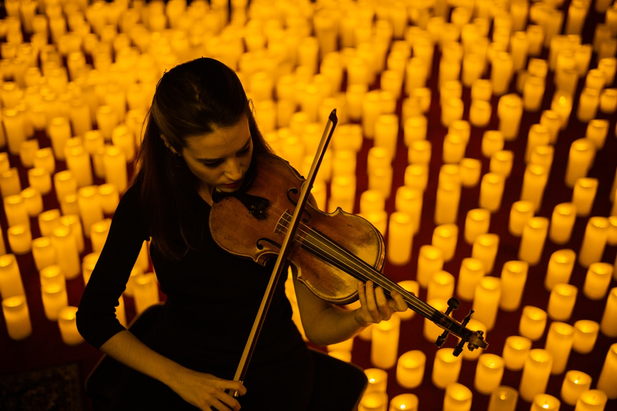 Una violinista tocando el violín rodeada de miles de velas