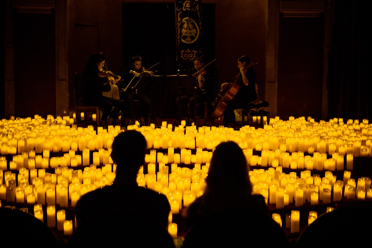 Asistentes sentados enfrente de un escenario a la luz de las velas mientras disfrutan de un concierto guiado por un cuarteto de cuerda