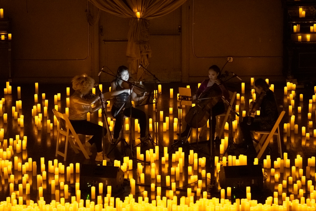 Un cuarteto de cuerda tocando los instrumentos en un escenario a oscuras y lleno de velas