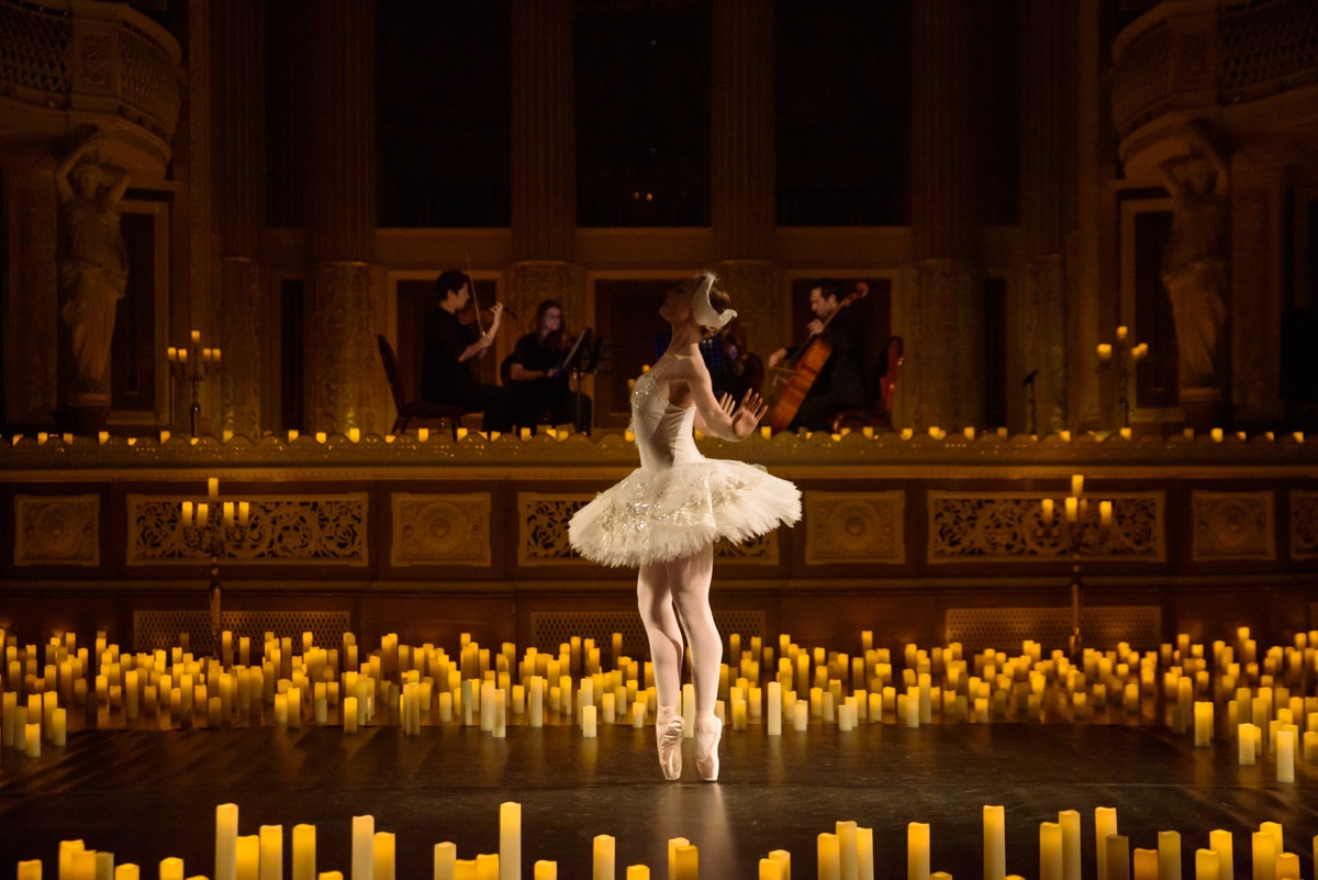 Un escenario lleno de velas con una bailarina de ballet en el medio y músicos al fondo