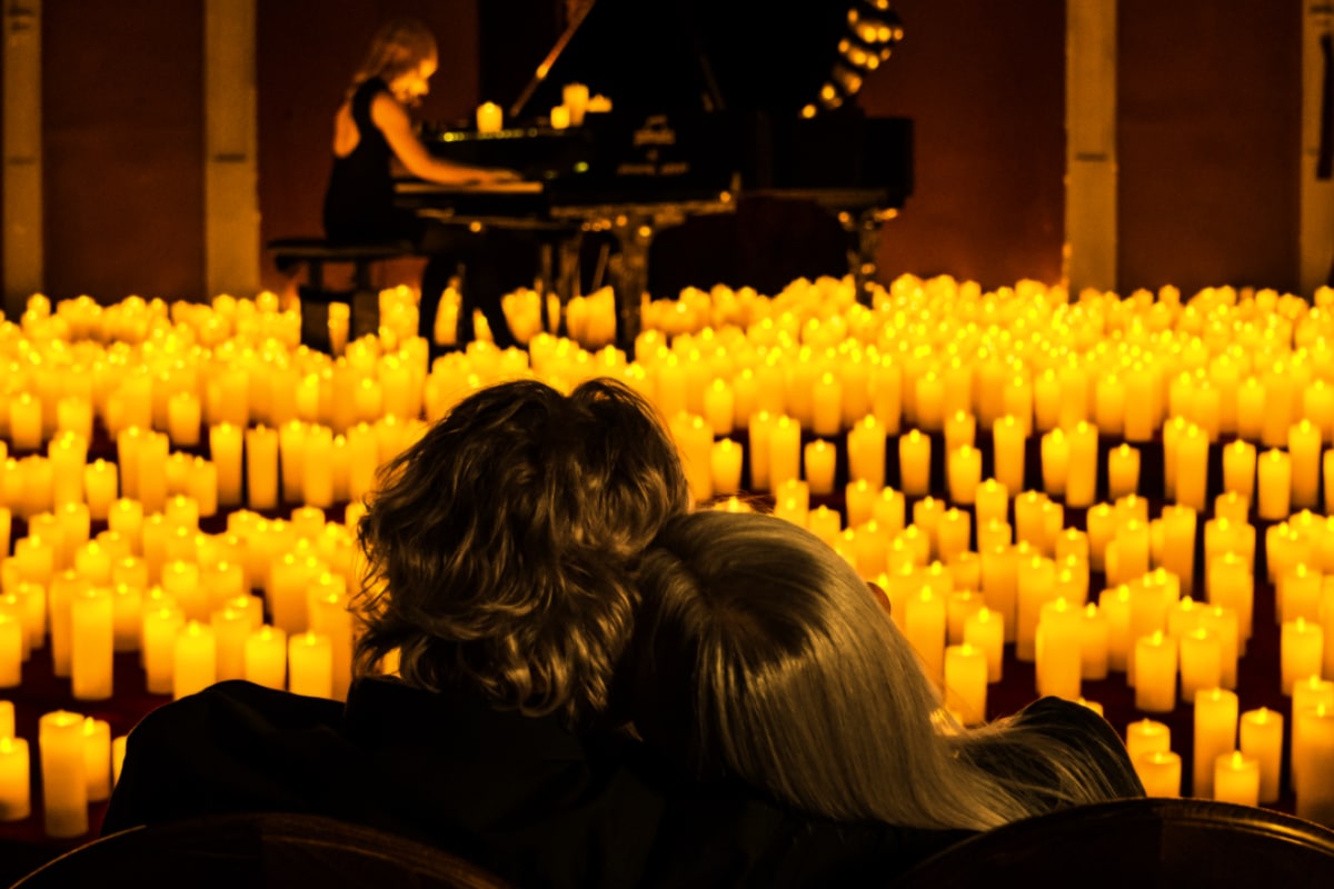 Dos personas apoyando sus cabezas en el otro mientras contemplan una pianista en un escenario lleno de velas