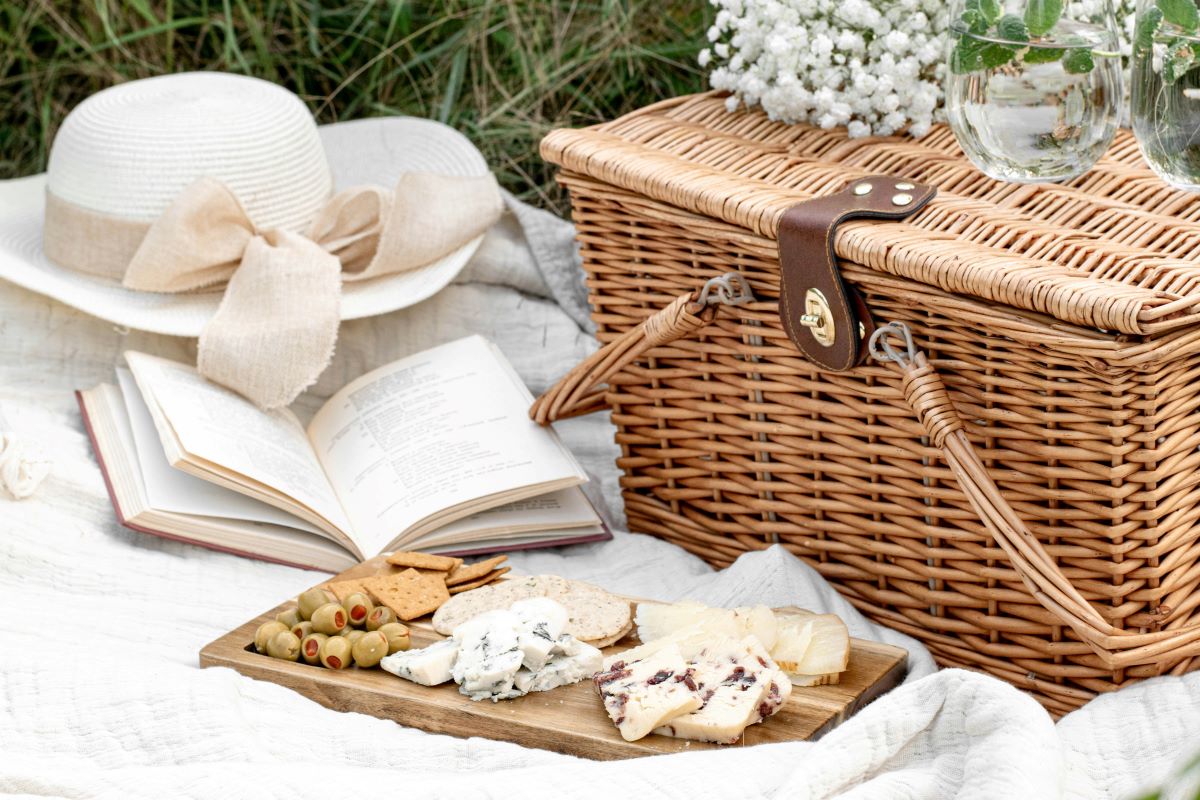 An image of a picnic basket and cheese board set up on a picnic blanket. 